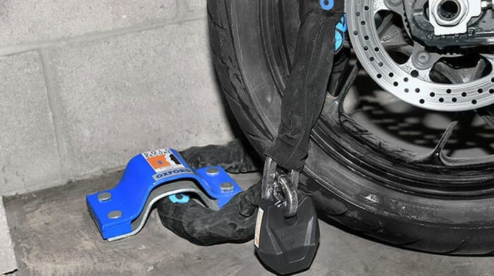 Motorcycle wheel with security chain and padlock fixed to ground anchor on floor